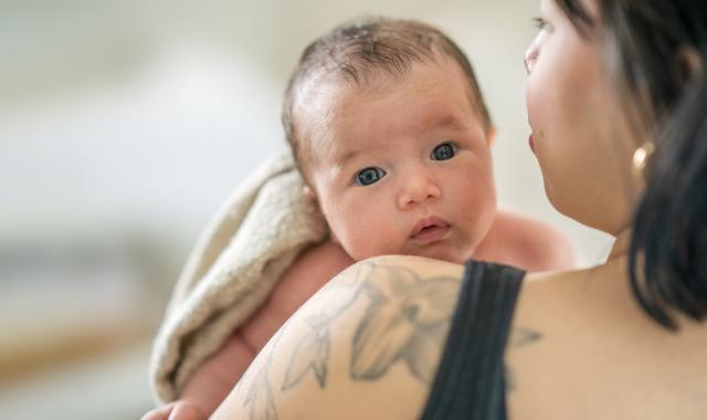 A baby looks over their mother's shoulder