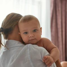 A baby looking over their mother's shoulder while being held.