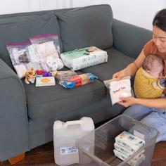 Woman with baby packing emergency supplies into a container.