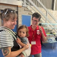 A mother with a baby in a carrier is supported by a volunteer in an evacuation centre.