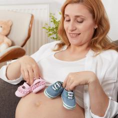 A pregnant woman holds two pairs of baby shoes