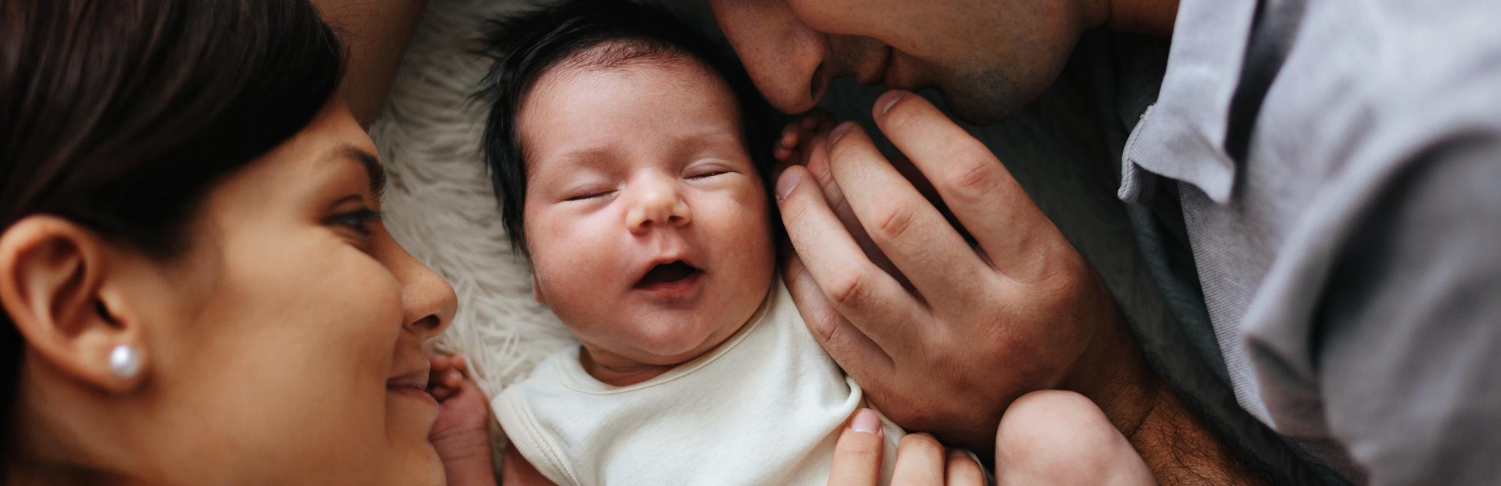 A mother and father smile at the newborn baby lying between them.